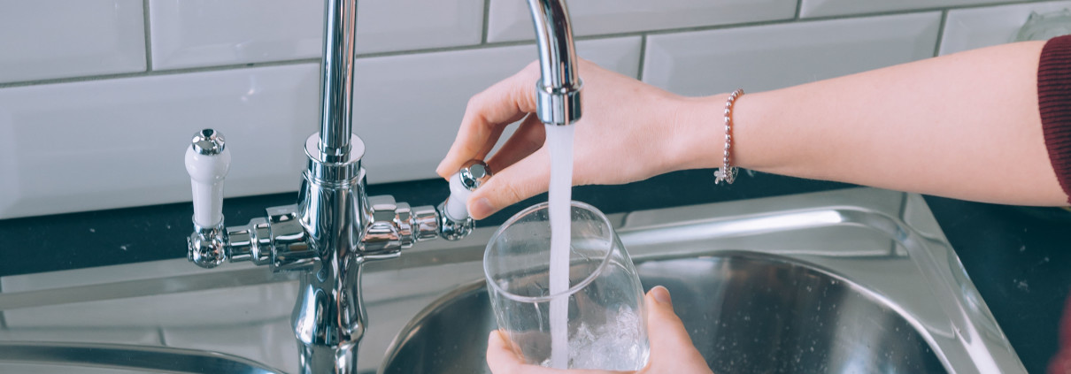 Woman filling the glass with water from the steel faucet in the kitchen